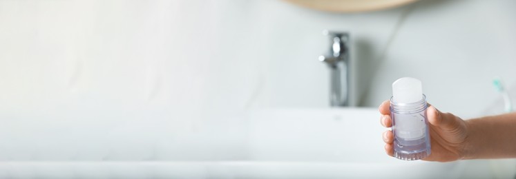 Image of Woman holding crystal alum deodorant in bathroom, closeup view with space for text. Banner design