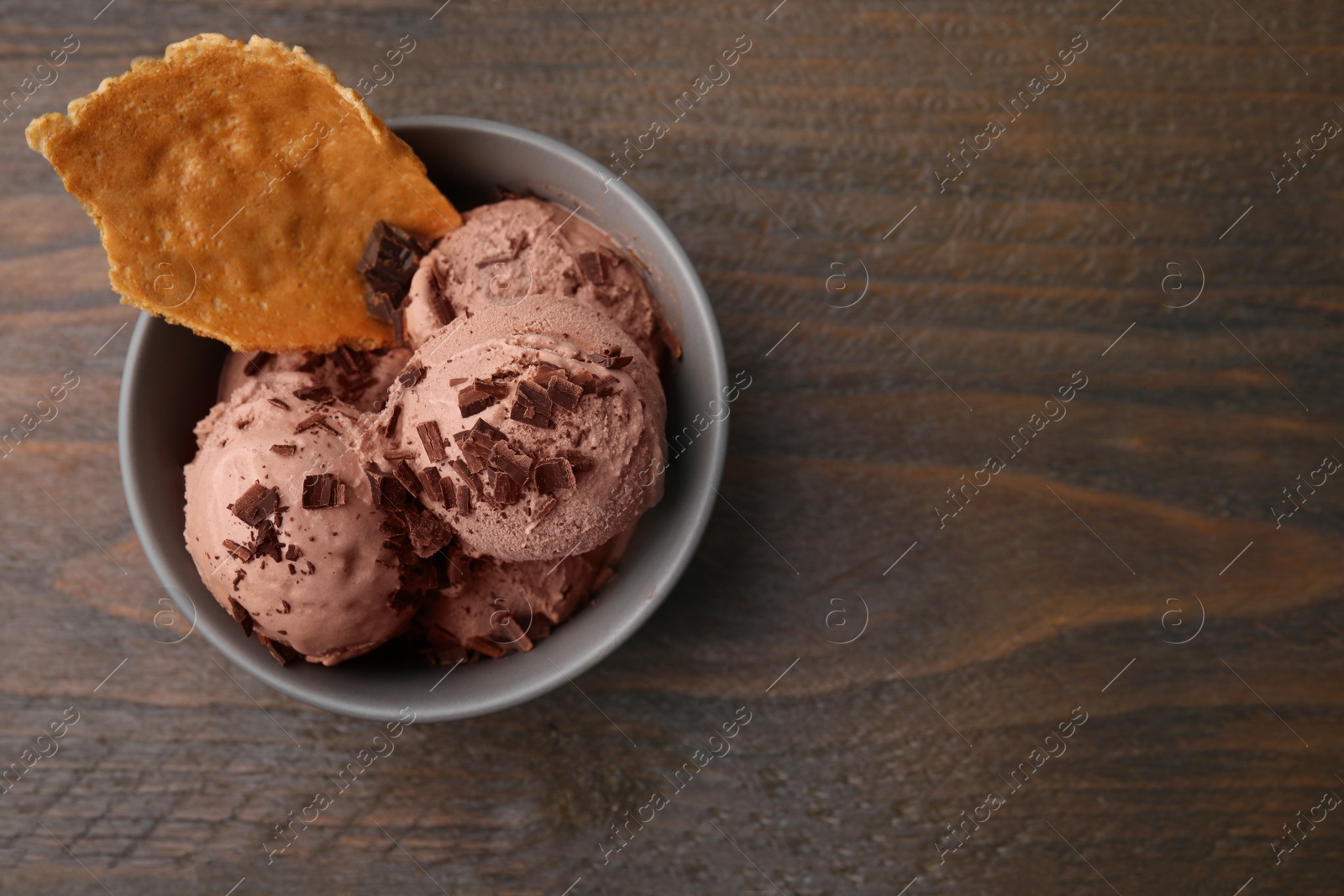 Photo of Tasty chocolate ice cream and piece of waffle cone in bowl on wooden table, top view. Space for text