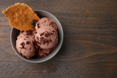 Photo of Tasty chocolate ice cream and piece of waffle cone in bowl on wooden table, top view. Space for text