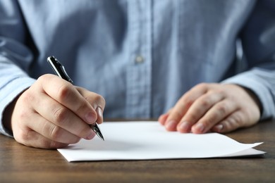 Man writing on sheet of paper with pen at wooden table, closeup