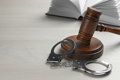 Judge's gavel, handcuffs and book on white wooden background. Criminal law concept