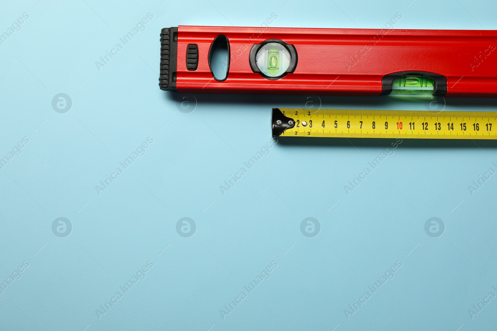 Photo of Building level and tape measure on light blue background, top view. Space for text