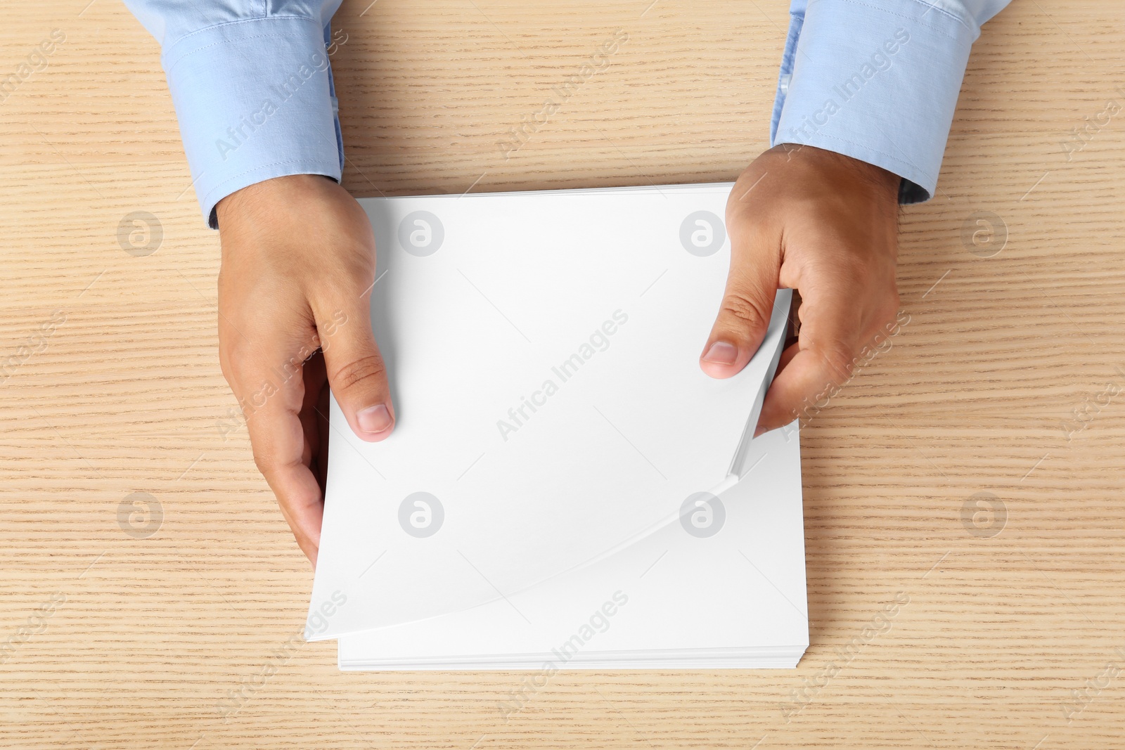 Photo of Man holding blank paper sheets for brochure at wooden table, top view. Mock up