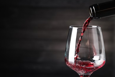 Photo of Pouring red wine into glass against dark background, closeup. Space for text