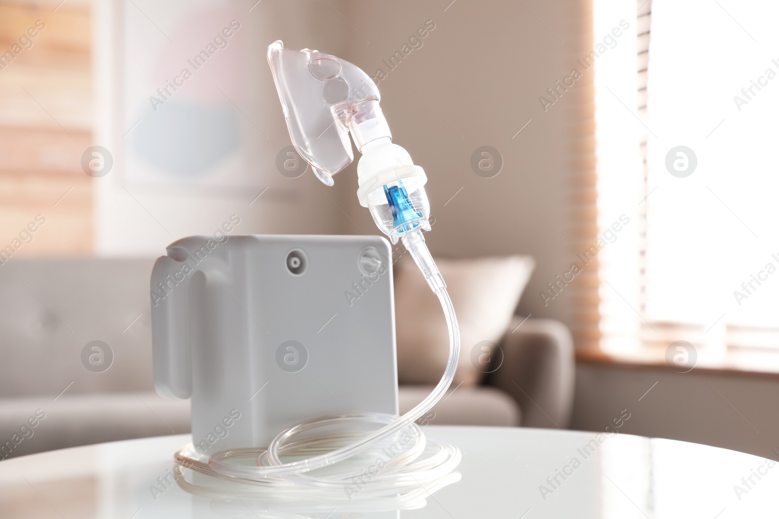 Photo of Modern nebulizer with face mask on white table indoors. Inhalation equipment