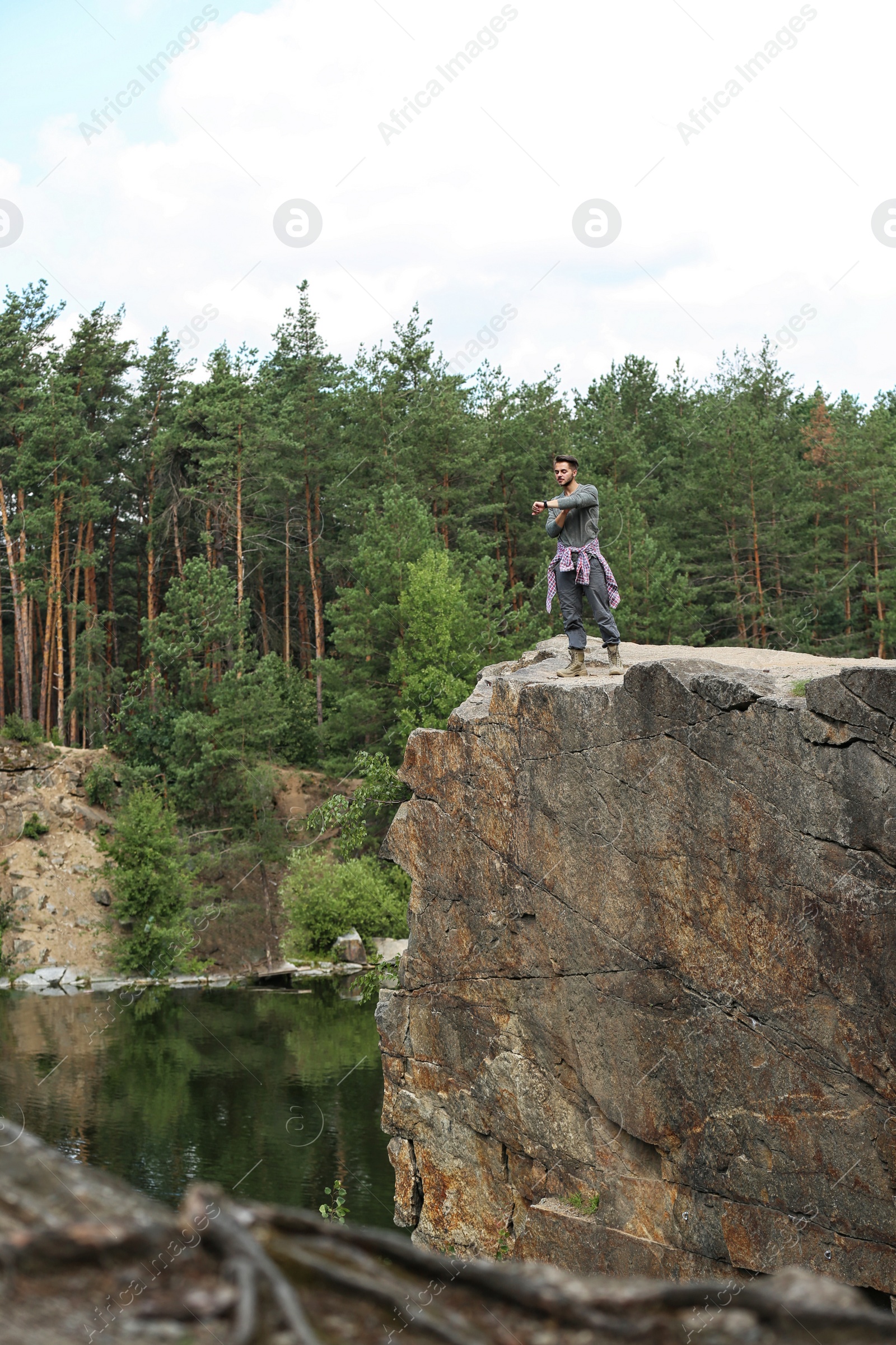 Photo of Young man on rock near lake and forest. Camping season