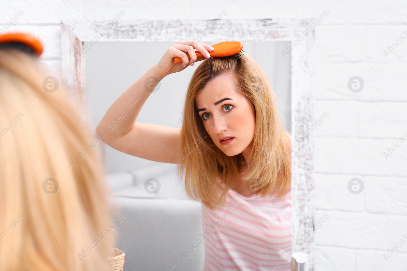 Photo of Emotional woman brushing hair near mirror in bathroom