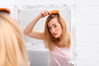 Photo of Emotional woman brushing hair near mirror in bathroom