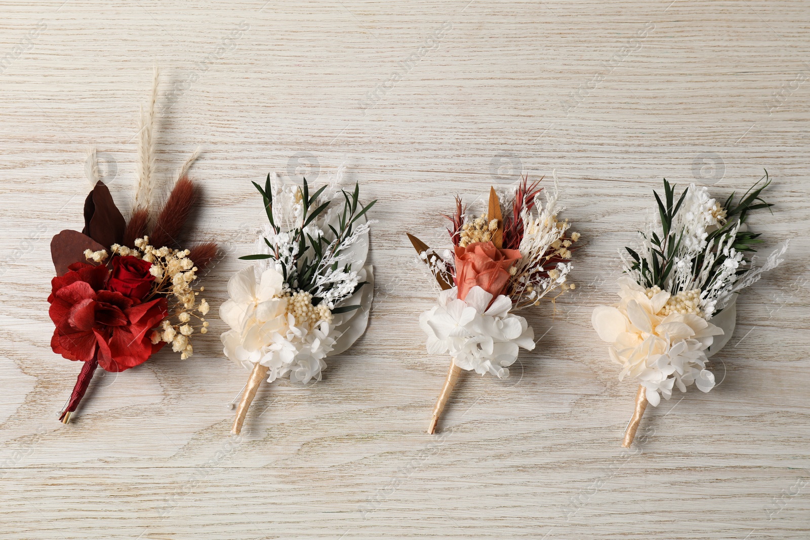 Photo of Stylish boutonnieres on white wooden table, flat lay