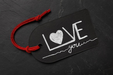 Photo of Tag with text I Love You and red rope on black background, top view