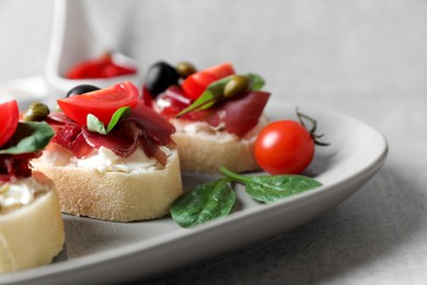 Photo of Delicious sandwiches with bresaola, cream cheese, olives and tomato on light grey table, closeup