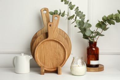 Photo of Wooden cutting boards, teapot, candle and vase with eucalyptus branches on white table
