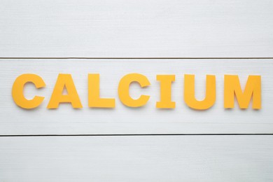 Photo of Word Calcium made of orange paper letters on white wooden table, top view
