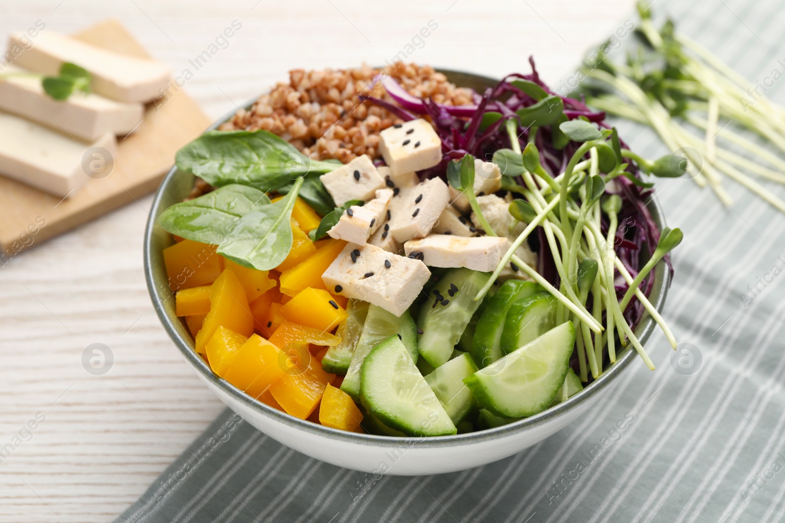 Photo of Delicious vegan bowl with bell pepper, tofu and cucumbers on wooden table, closeup