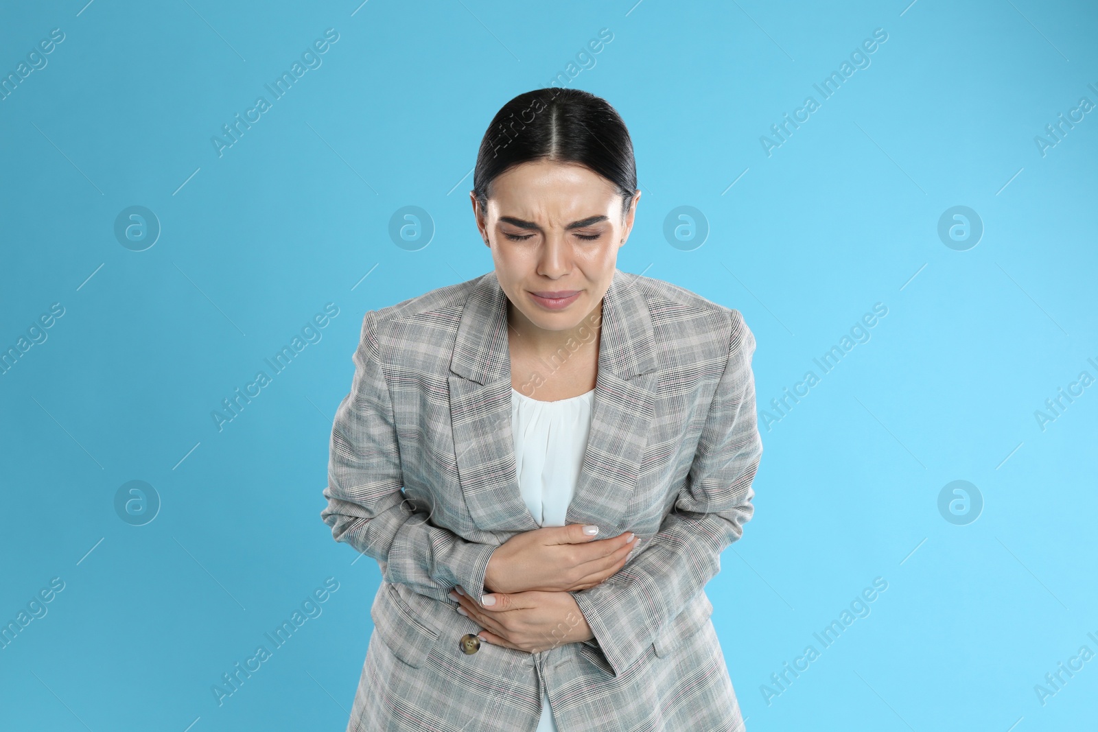 Photo of Woman in office suit suffering from stomach ache on light blue background. Food poisoning