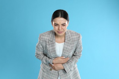Woman in office suit suffering from stomach ache on light blue background. Food poisoning