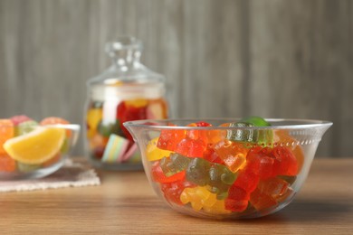 Different delicious gummy candies in glass bowl on wooden table