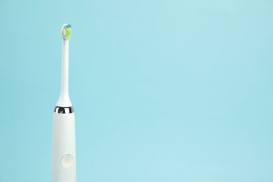 Electric toothbrush on light blue background, space for text