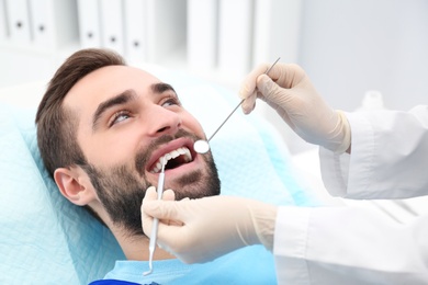 Dentist examining young man's teeth with mirror and probe in hospital