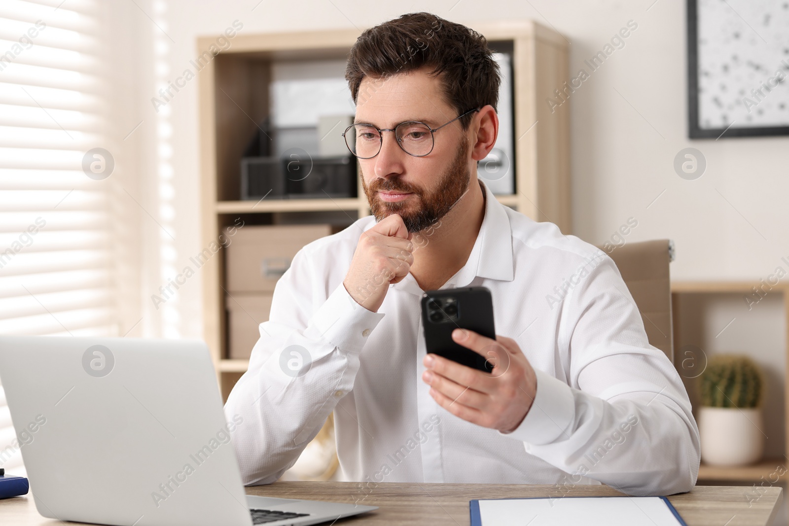 Photo of Handsome man with smartphone using laptop at table in office