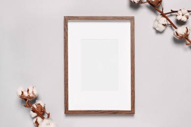 Photo of Empty photo frame and dry cotton branches with fluffy flowers on light background, flat lay. Space for design