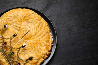 Photo of Traditional galette des rois with crown on black table, top view. Space for text