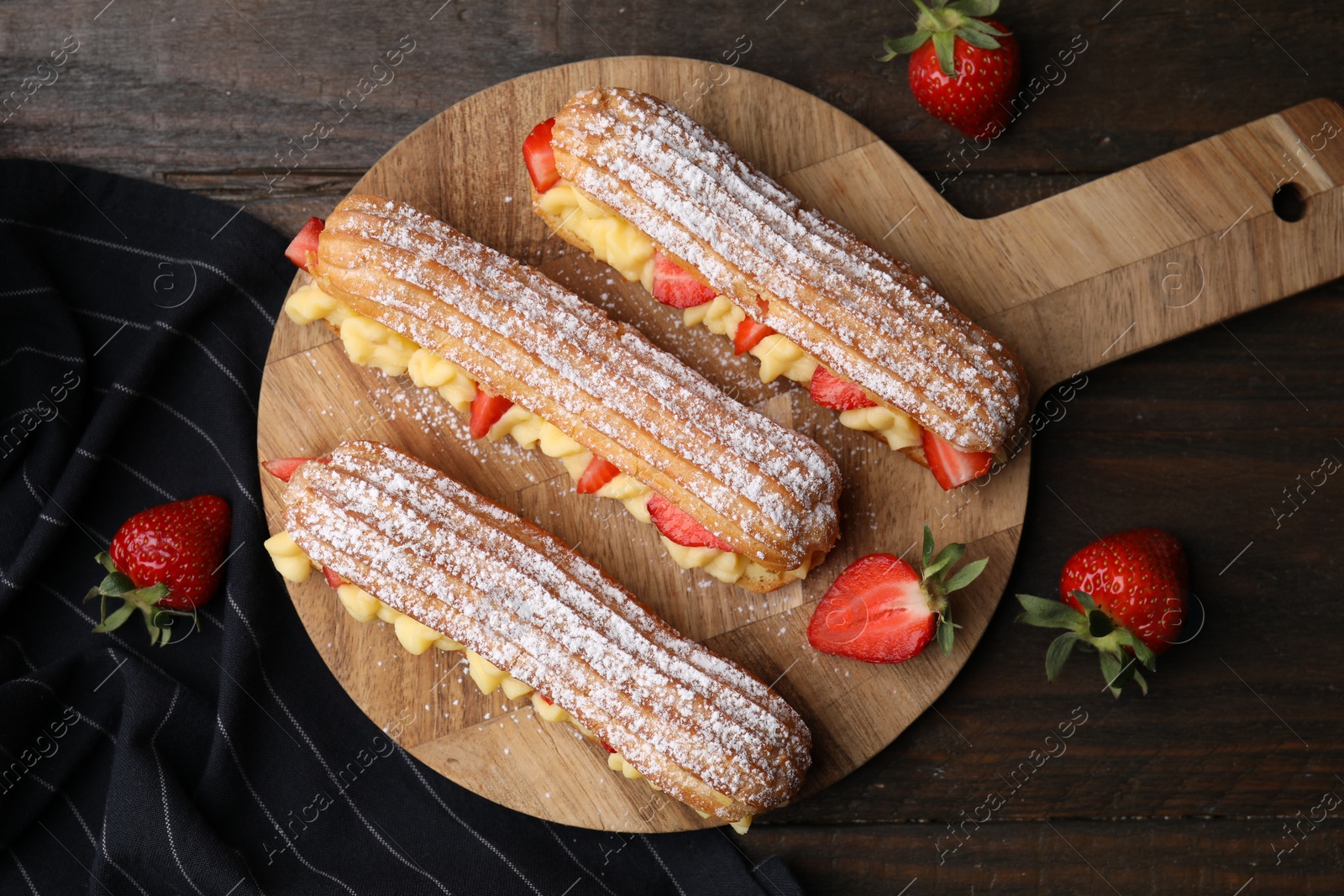 Photo of Delicious eclairs filled with cream and strawberries on wooden table, top view