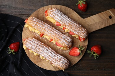 Photo of Delicious eclairs filled with cream and strawberries on wooden table, top view