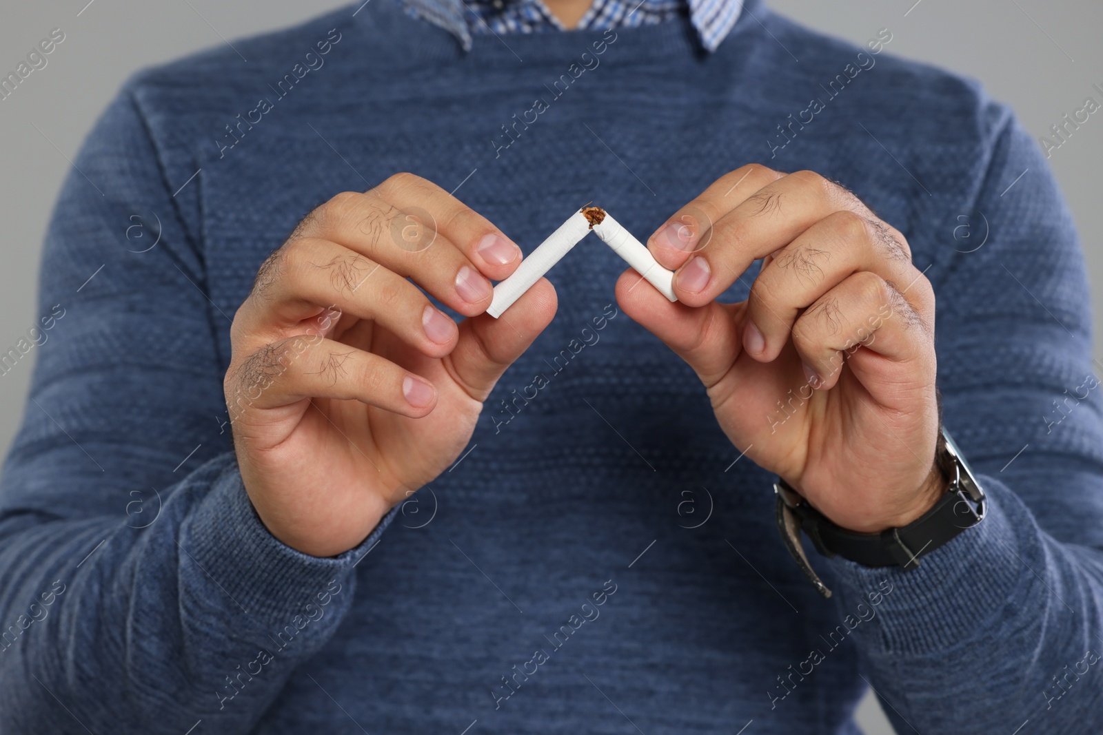 Photo of Stop smoking concept. Man breaking cigarette on light grey background, closeup