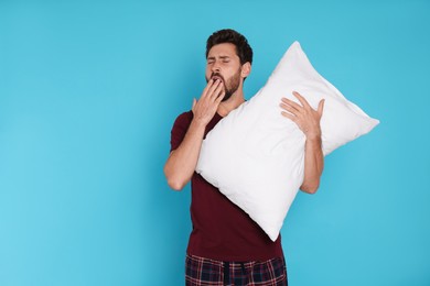 Tired man with pillow yawns on light blue background, space for text