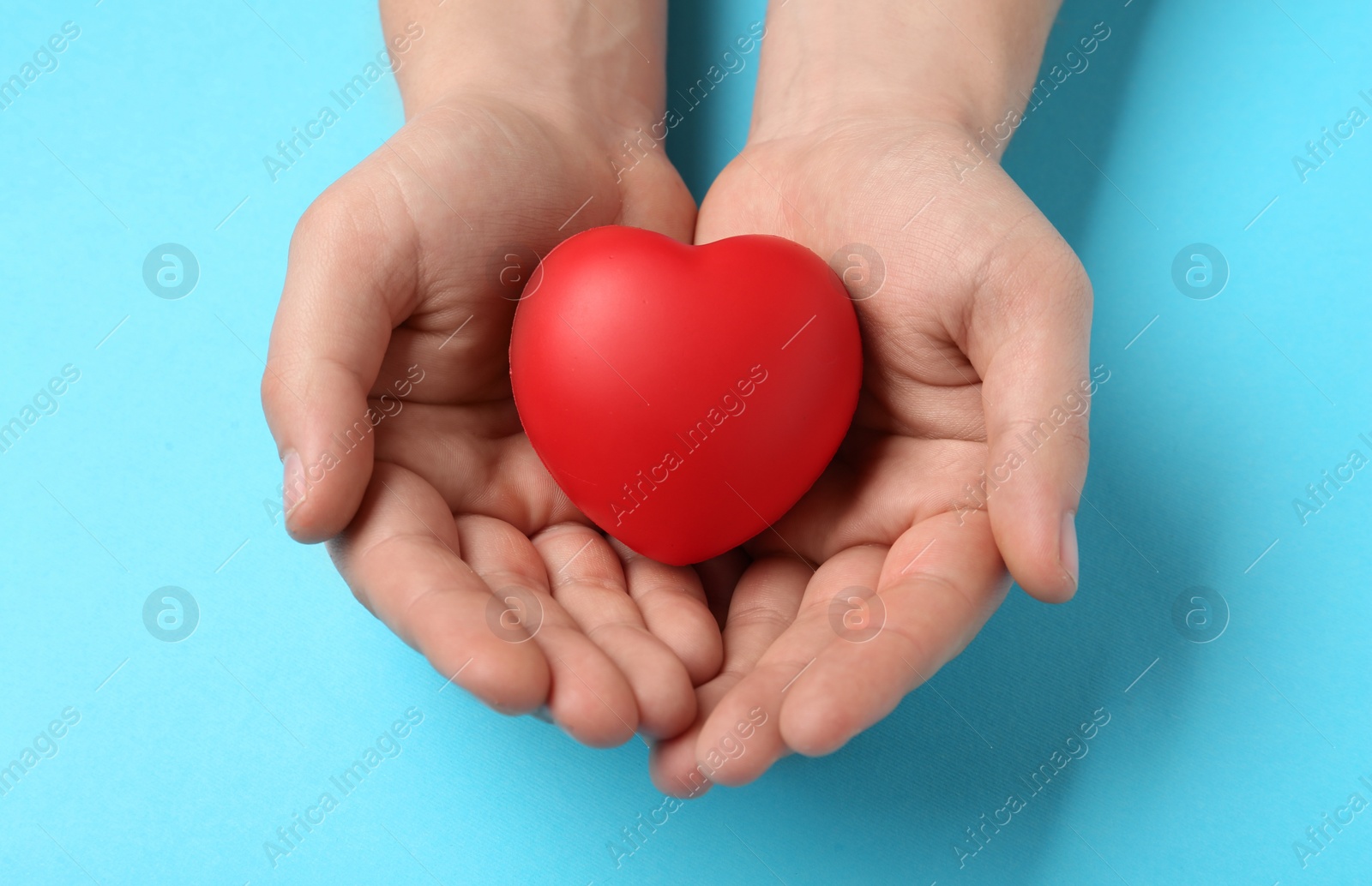 Photo of Man holding red decorative heart on light blue background, top view. Cardiology concept
