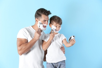 Photo of Father and son shaving on color background