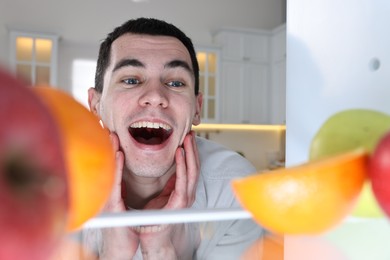 Photo of Happy man near refrigerator in kitchen, view from inside