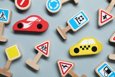 Photo of Set of wooden road signs and cars on light grey background, flat lay. Children's toy