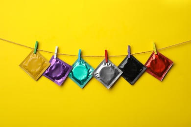 Photo of Colorful condoms hanging on clothesline against yellow background. Safe sex concept