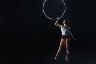 Photo of Young woman performing acrobatic element on aerial ring against dark background. Space for text