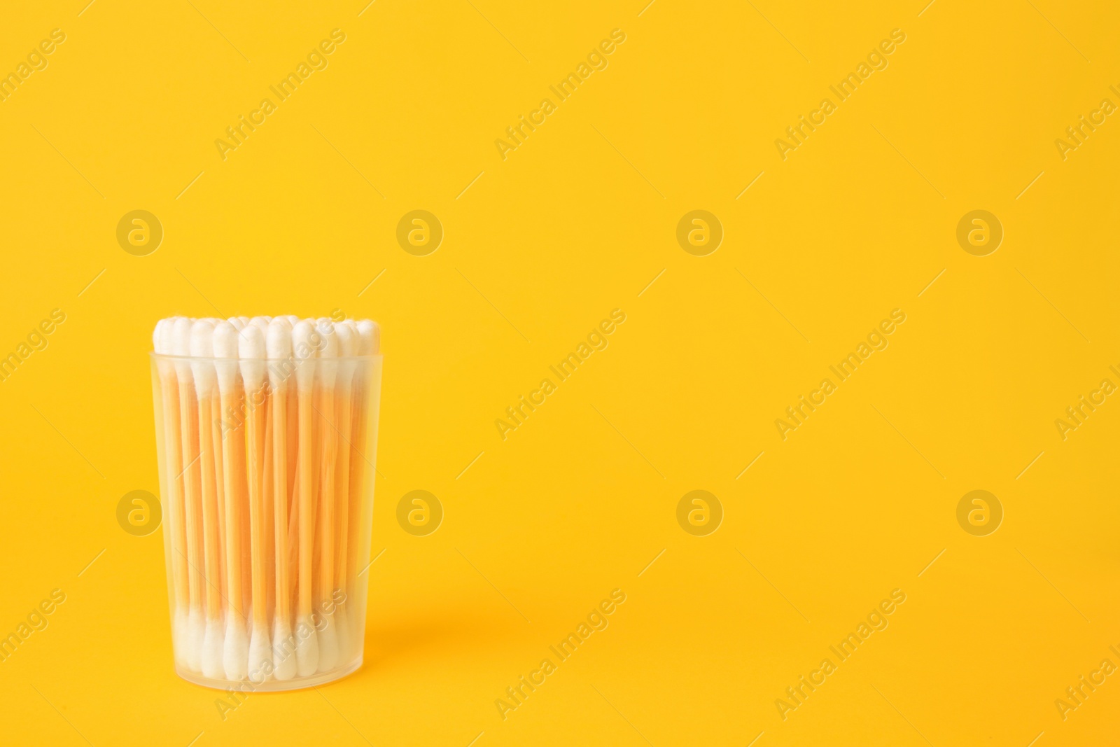 Photo of Container with new cotton buds on yellow background. Space for text