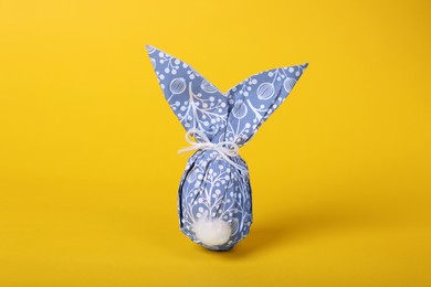 Photo of Easter bunny made of wrapping paper and egg on yellow background