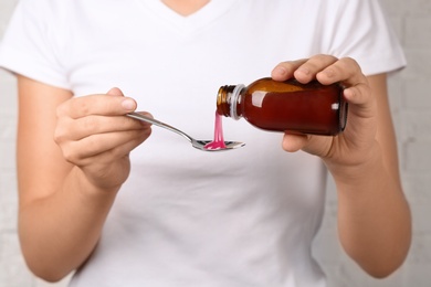 Photo of Woman pouring cough syrup into spoon, closeup