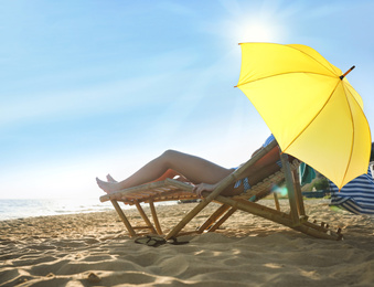 Image of Young couple relaxing in deck chairs under umbrella for sun protection on beach near sea