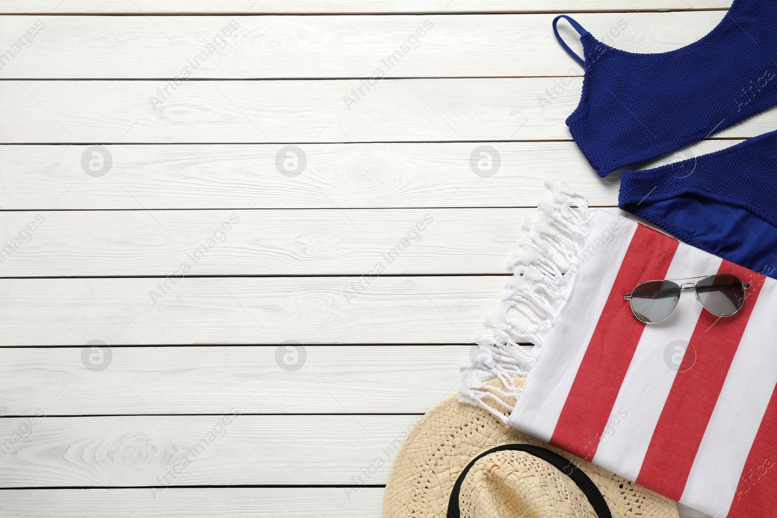 Photo of Beach towel, swimsuit, sunglasses and hat on white wooden background, flat lay. Space for text