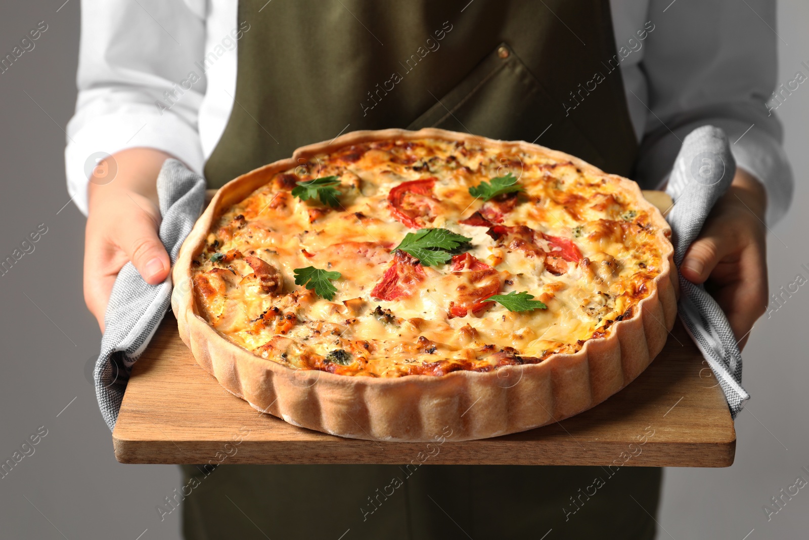 Photo of Woman holding board with tasty quiche on grey background, closeup