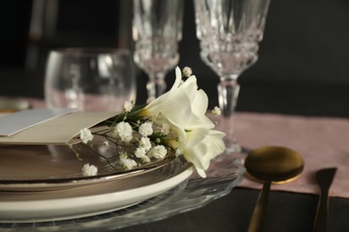 Stylish table setting. Plates, cutlery and floral decor on black surface, closeup with space for text