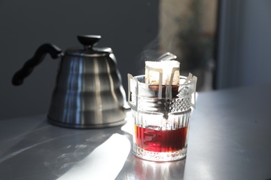 Photo of Glass with drip coffee bag and kettle on light grey table