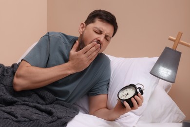 Photo of Sleepy man with alarm clock in bed at home