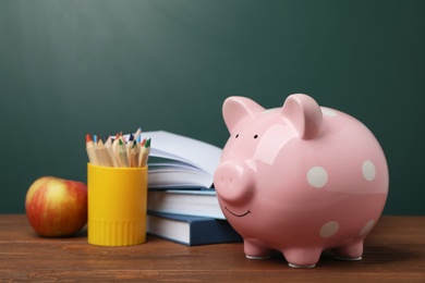 Photo of Piggy bank with stack of books and apple on table