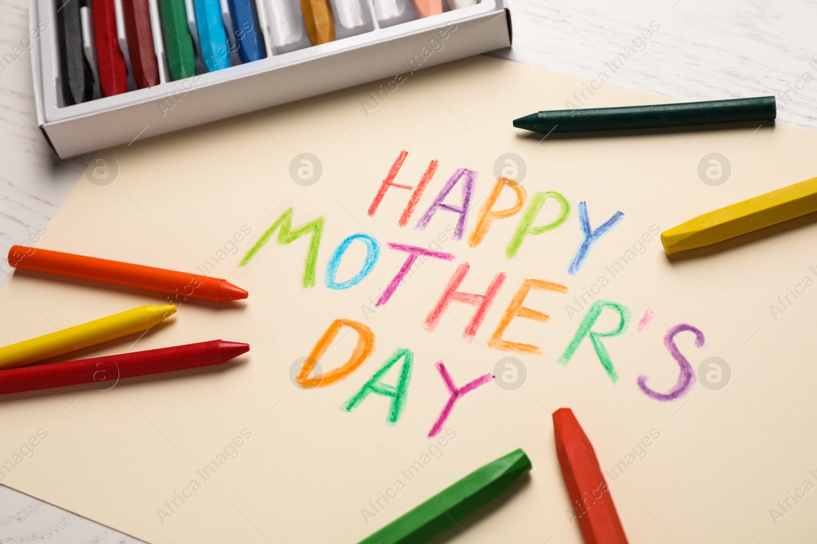 Photo of Handmade greeting card for Mother's Day and crayons on light wooden table, closeup