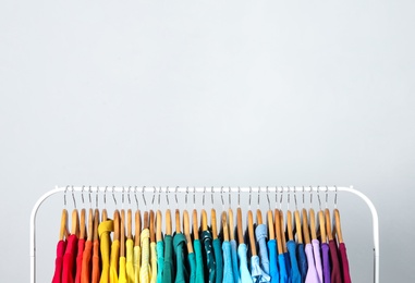 Photo of Rack with bright clothes on light blue background. Rainbow colors