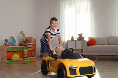 Photo of Cute little boy playing with big toy car and stuffed bunny at home
