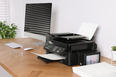Photo of Modern printer with paper near computer on wooden table in office